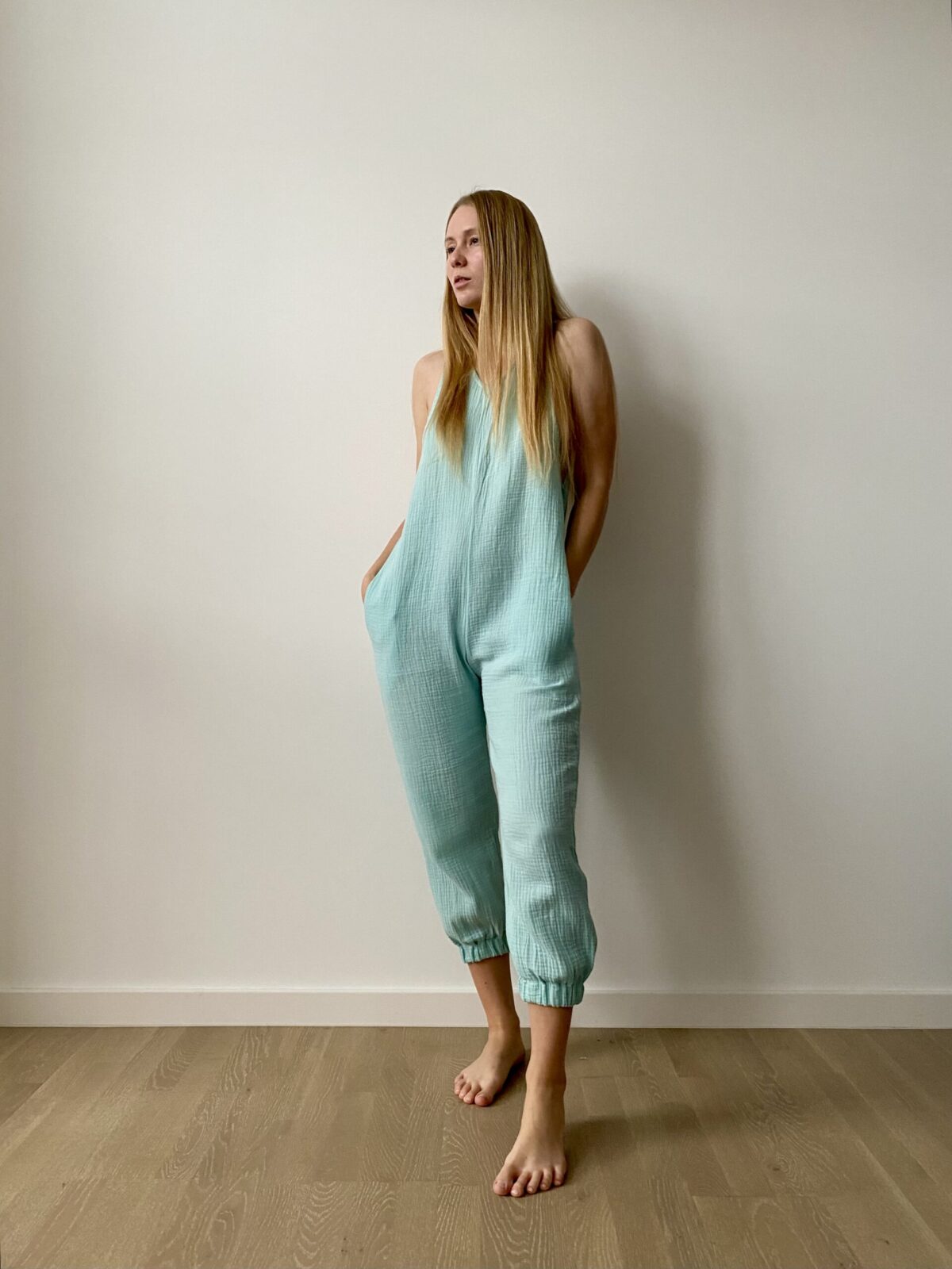 Woman wearing an organic muslin lounge jumpsuit in airy cotton with relaxed fit, pockets, and minimalist design.