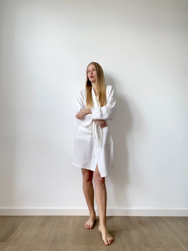 Woman in white cotton muslin robe with a wrap tie and pockets, perfect for everyday softness and ease.