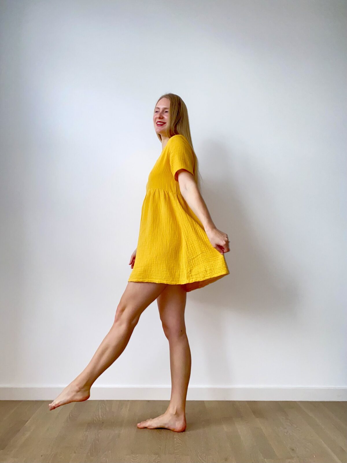 Woman in a short-sleeve muslin babydoll mini dress twirling with a relaxed, flowy silhouette.