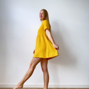 Woman in a short-sleeve muslin babydoll mini dress twirling with a relaxed, flowy silhouette.