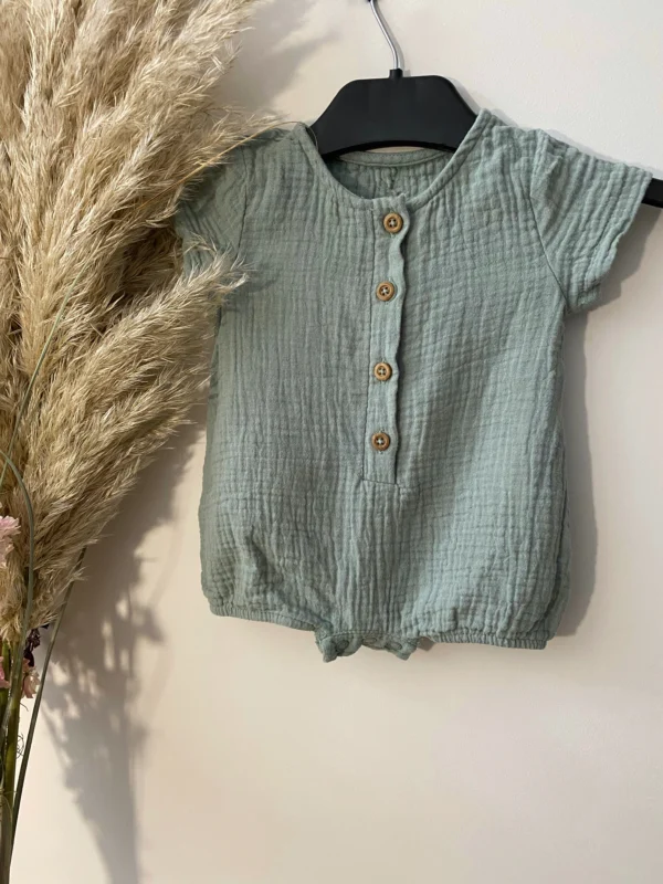 Natural cotton muslin jumpsuit for babies with short sleeves, wooden buttons, and soft gathered legs.