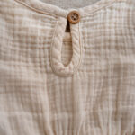 long-sleeve baby dress in natural muslin with gathered waist and frill details