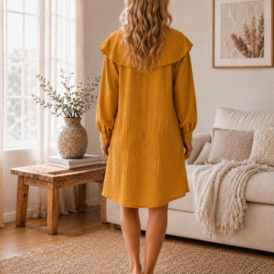 Woman wearing a mustard cotton muslin shirt dress with ruffle collar, long sleeves and button back